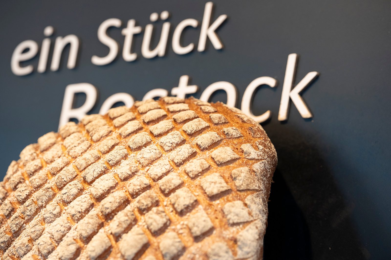 Frisch gebackenes Brot vor dem Schriftzug „ein Stück Rostock“ — Brotzeit Rostock